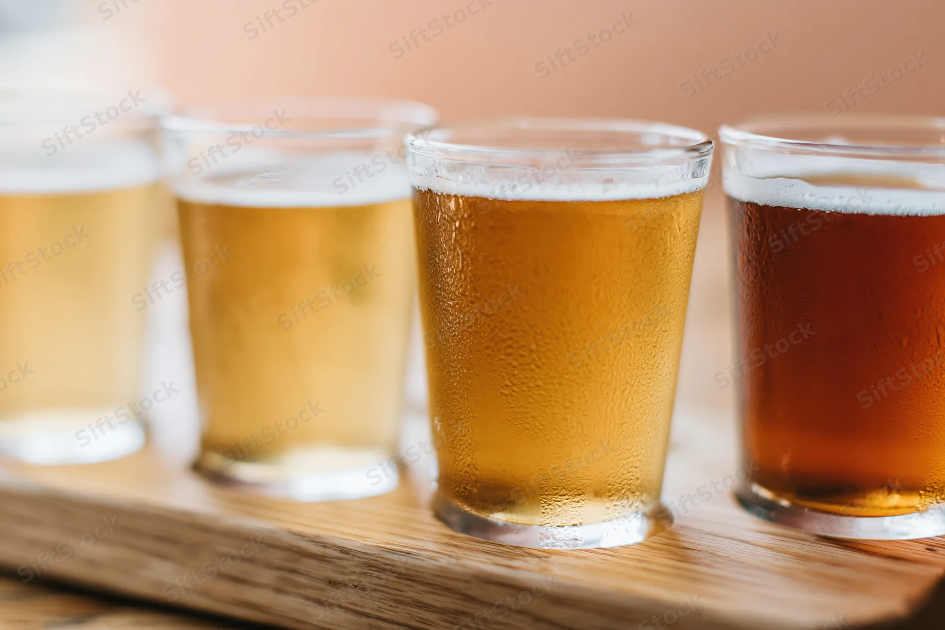Four craft beers in small pint glasses arranged on a wooden tray with condensation and foam