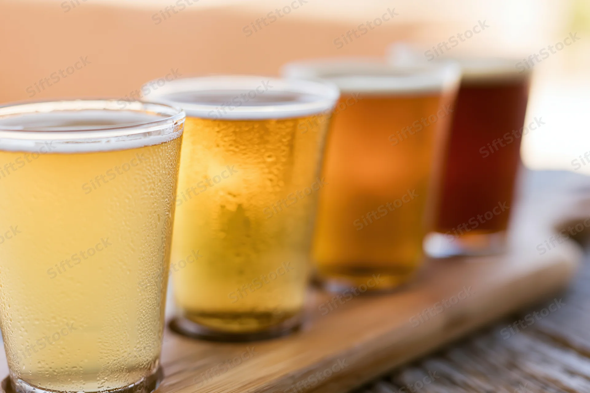 Four craft beers in small pint glasses arranged on a wooden tray with condensation and foam, showcasing variety in color and type