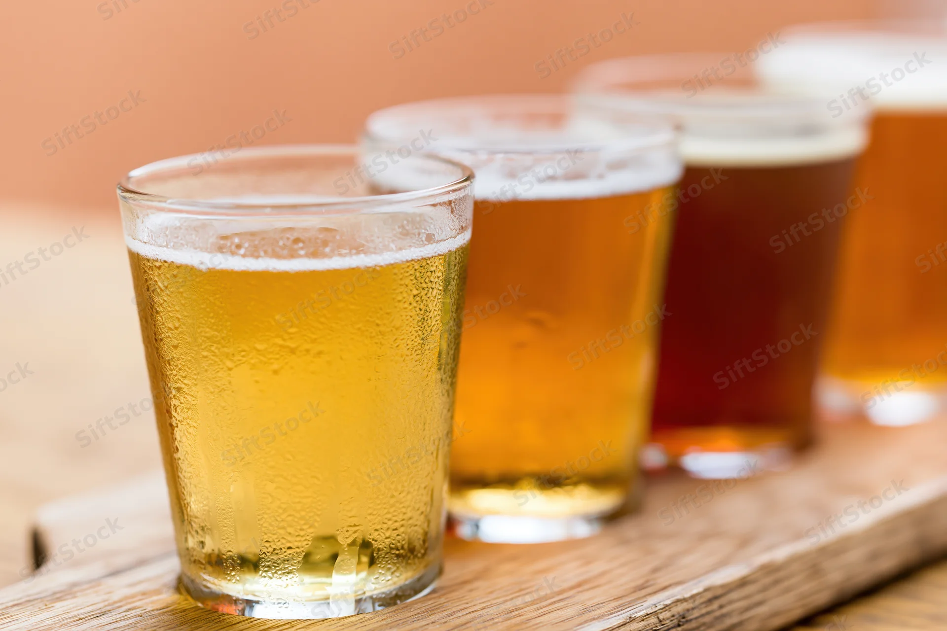 Four craft beers in pint glasses arranged on a wooden tray with condensation and foam