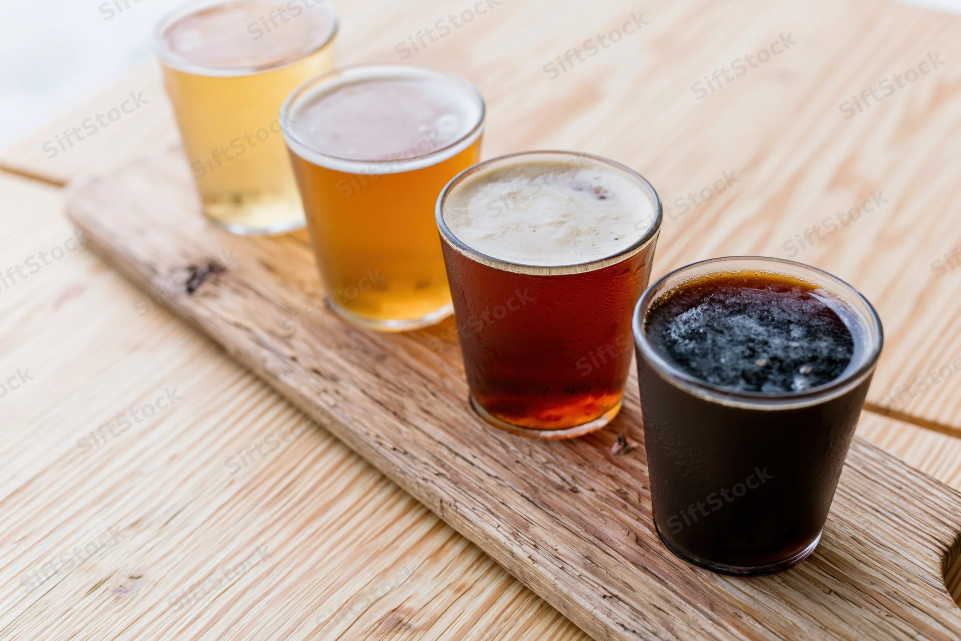 Four small beer tasting glasses arranged diagonally on a wooden serving board