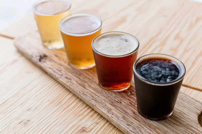 Four small beer tasting glasses arranged diagonally on a wooden serving board