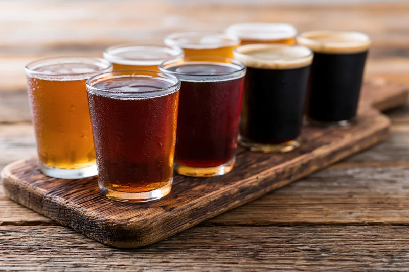 Seven craft beers in glasses arranged on a rustic wooden tray