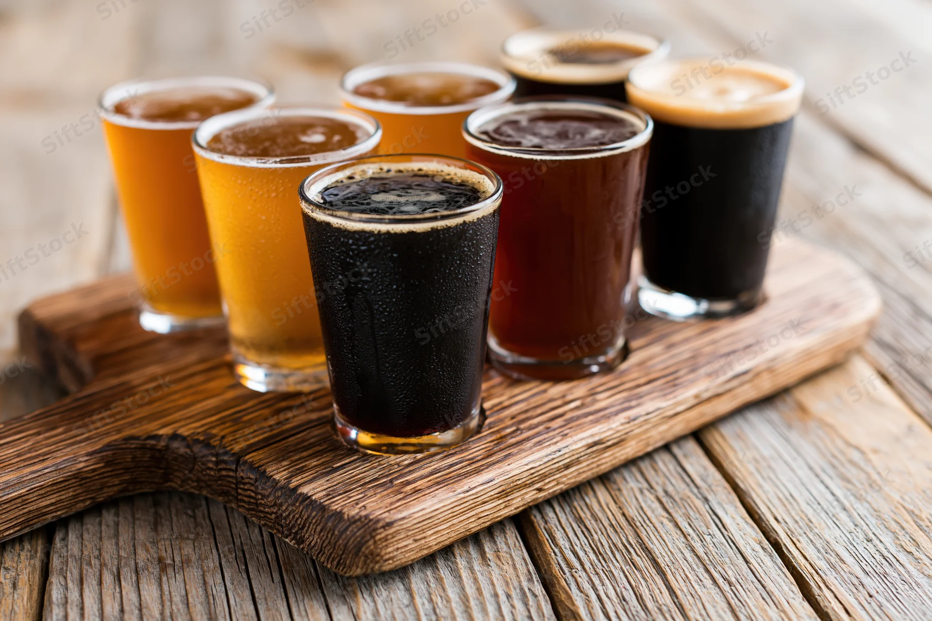 Seven craft beers in glasses arranged on a wooden serving tray