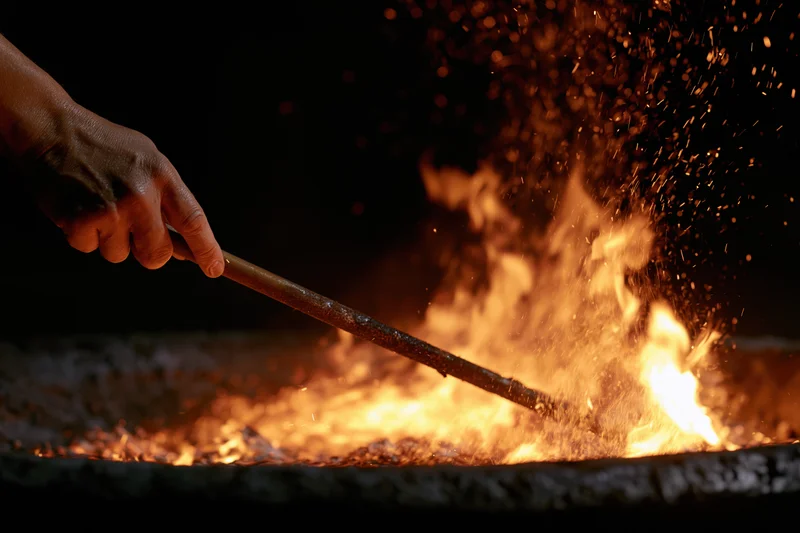 Hand stirring flames in a metal fire pit at night