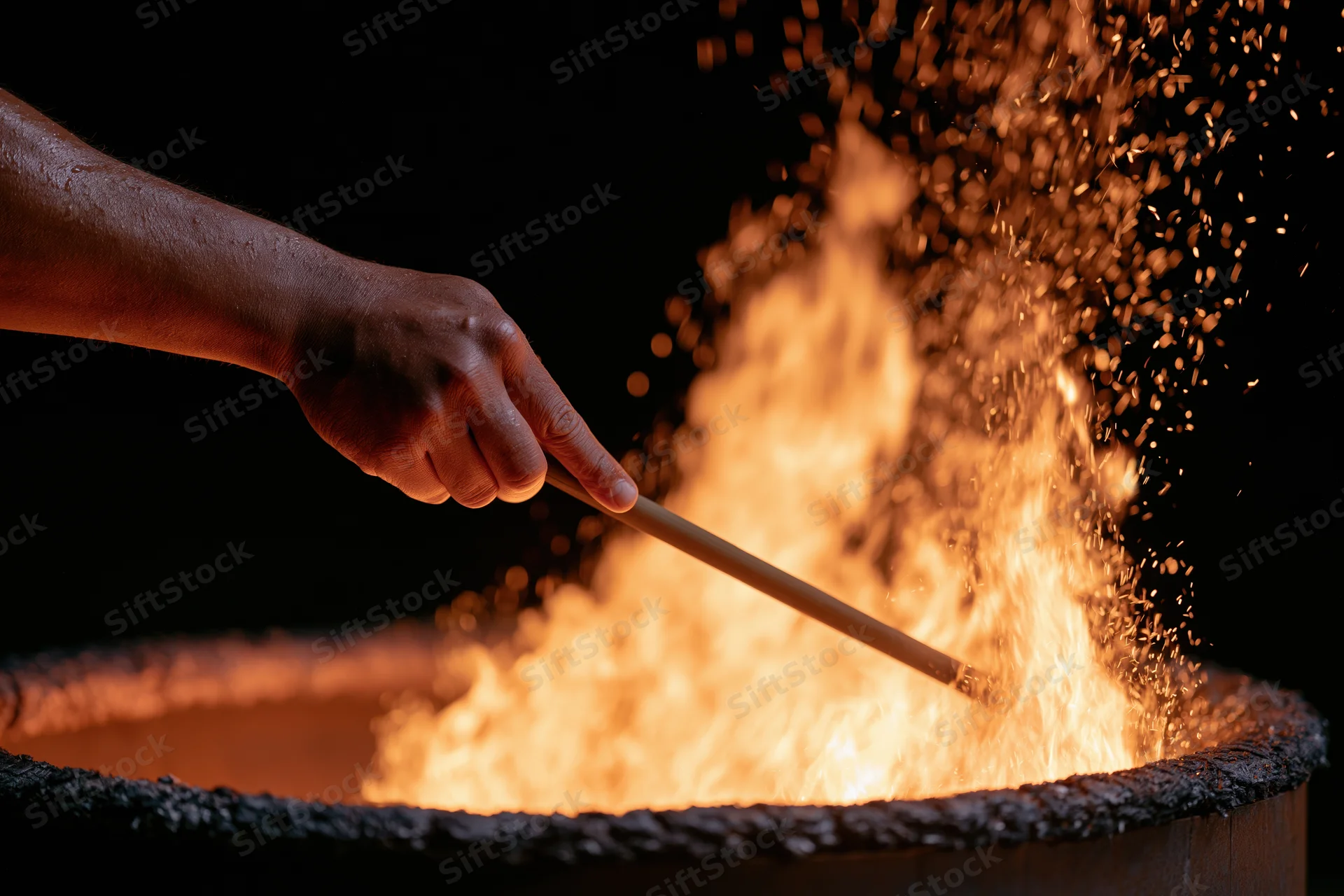Hand stirring flames in a metal fire pit with sparks flying