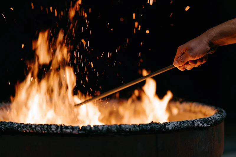 Hand stirring flames in a metal fire pit at night