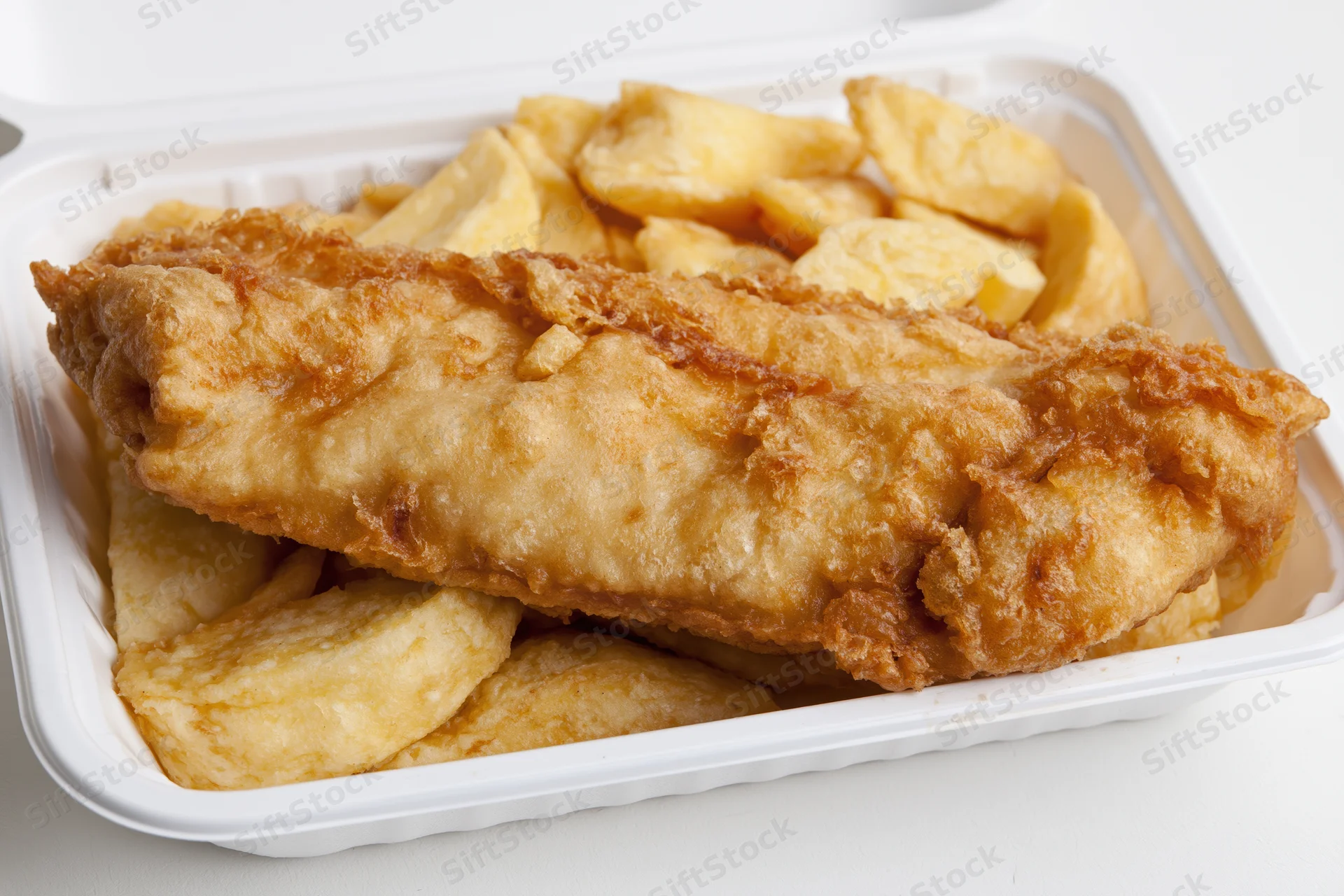 Battered fish fillet resting on thick-cut chips in a white takeaway container