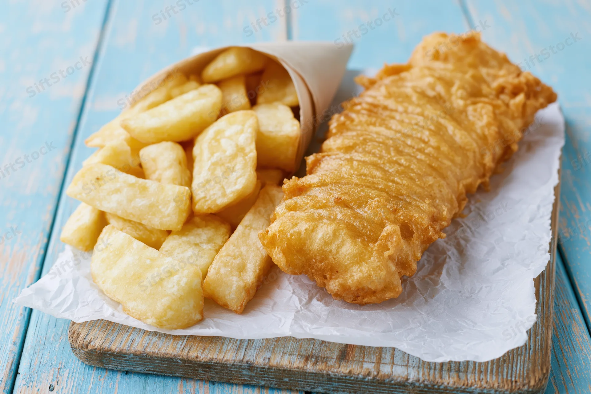 Golden battered fish fillet and thick-cut chips on crumpled paper atop a wooden board