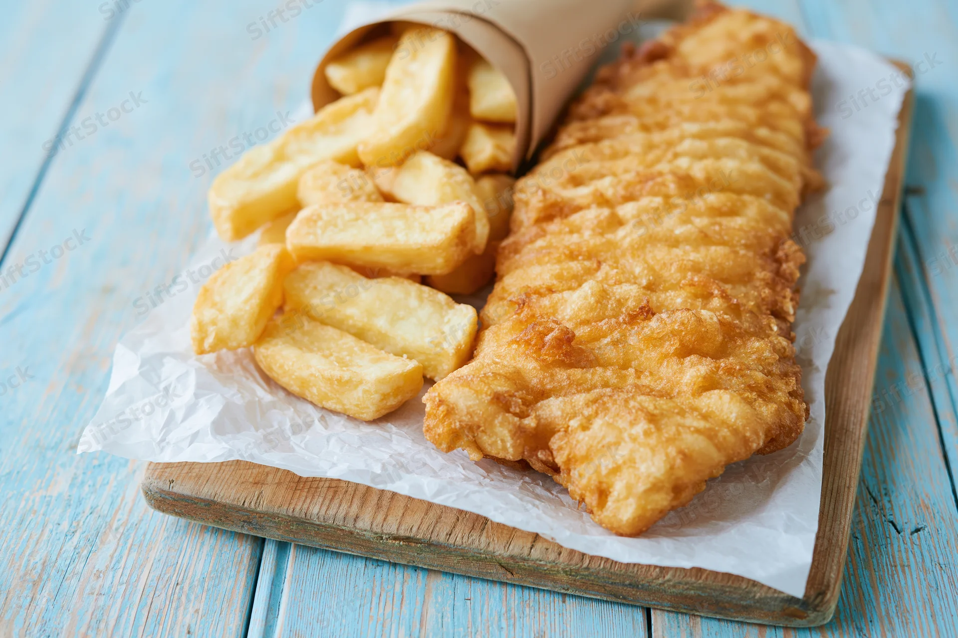 Golden battered fish fillet with thick-cut chips on parchment paper on a wooden board