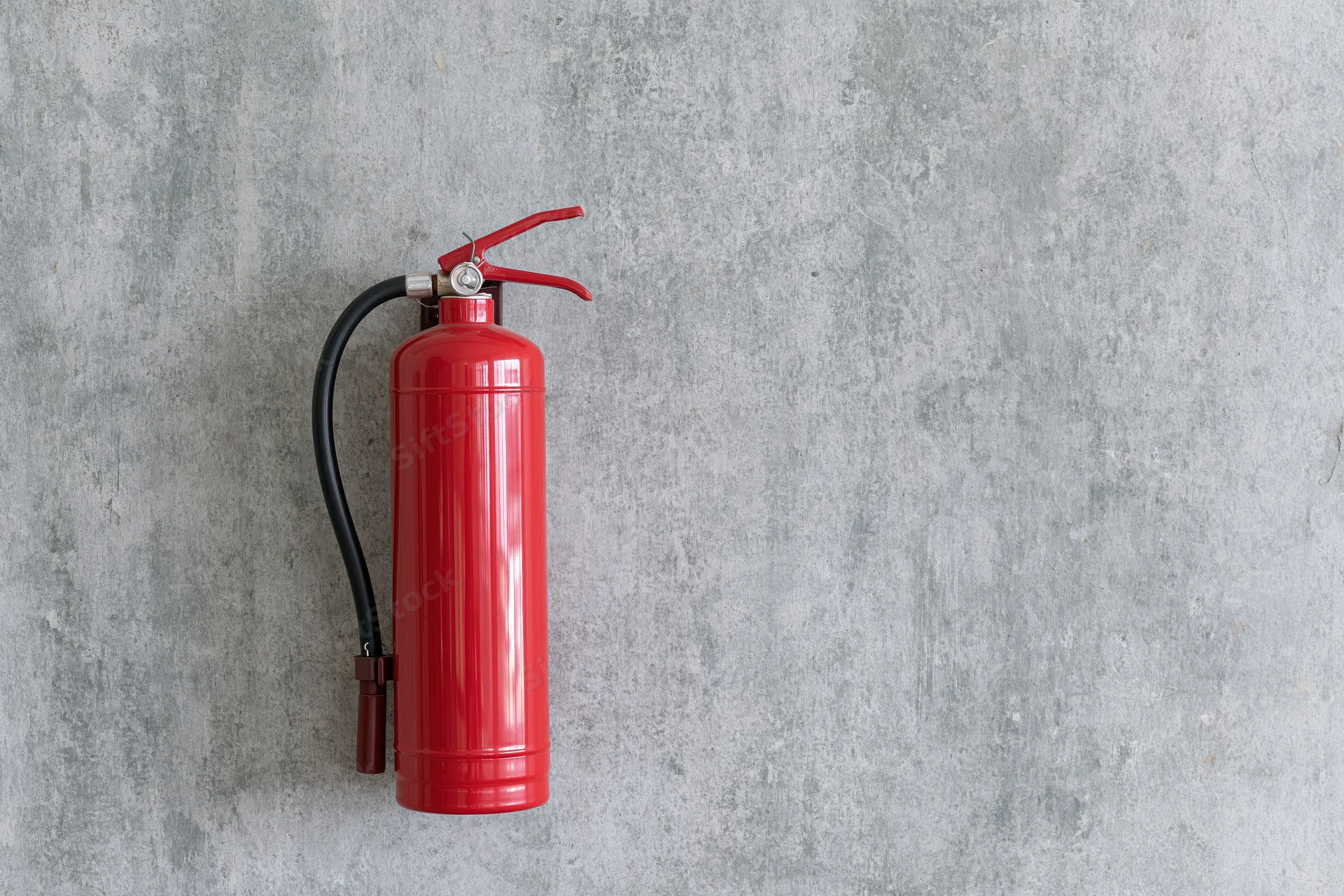 Red fire extinguisher mounted on a rough concrete wall