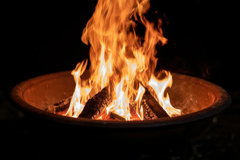 Tall flames burning in a round metal fire pit at night