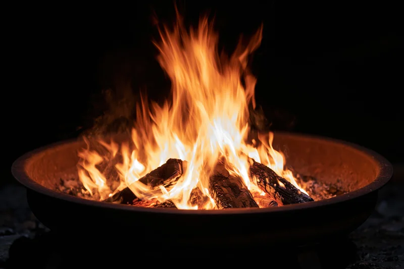Tall flames burning in a round metal fire pit at night