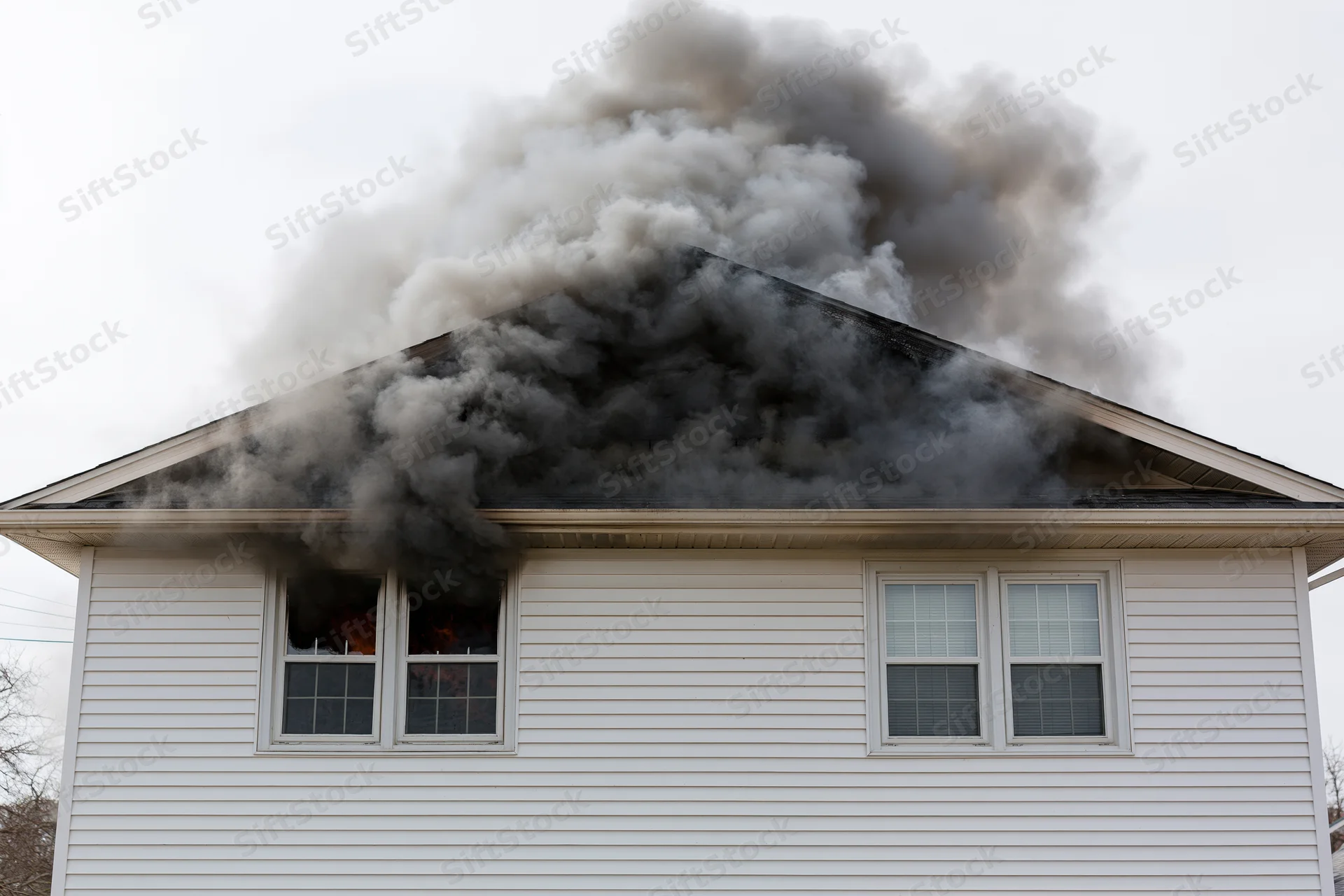 Burning single-story house with thick smoke billowing from roof and window