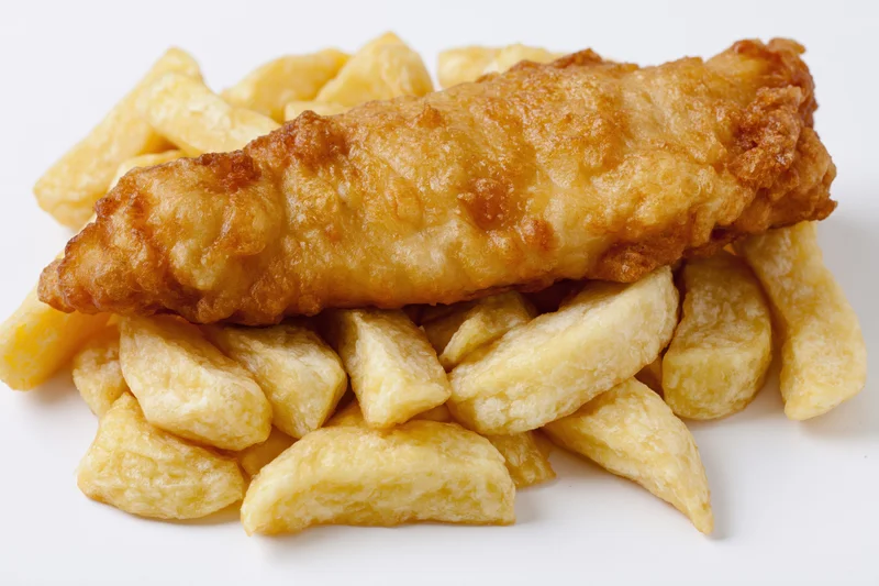 Battered fish fillet resting on thick-cut chips against white background