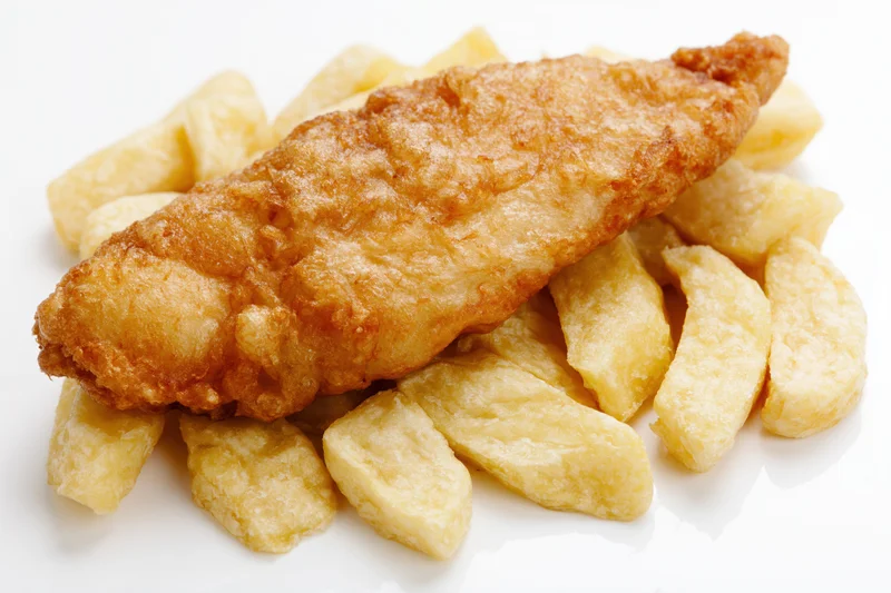 Battered fish fillet resting on thick-cut chips on a white surface