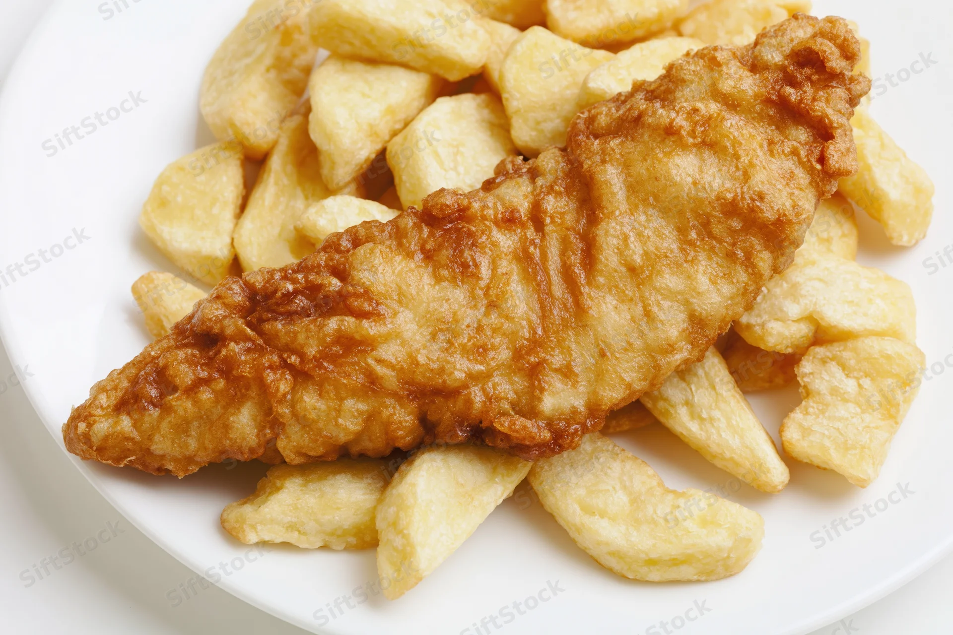 Battered fish fillet on a pile of thick-cut chips on a white plate