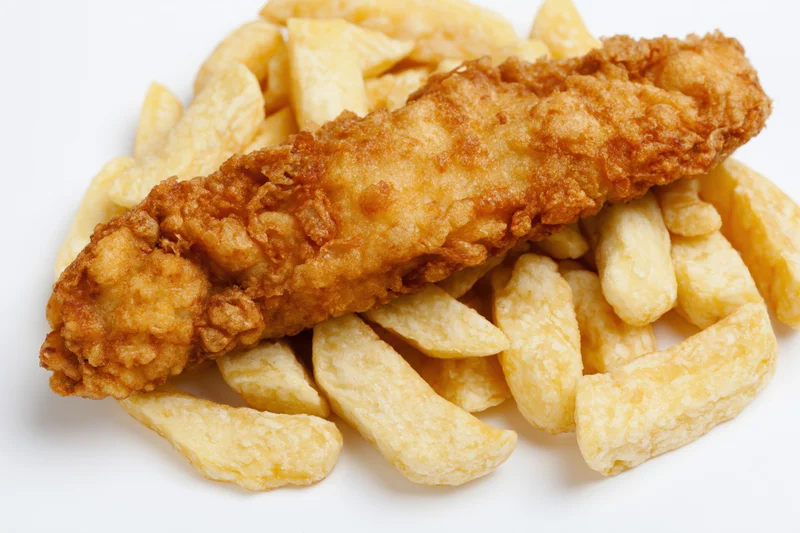 Battered fish fillet resting on thick-cut chips against white background