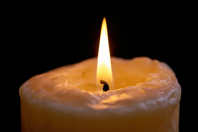A lit candle with a steady flame against a dark background