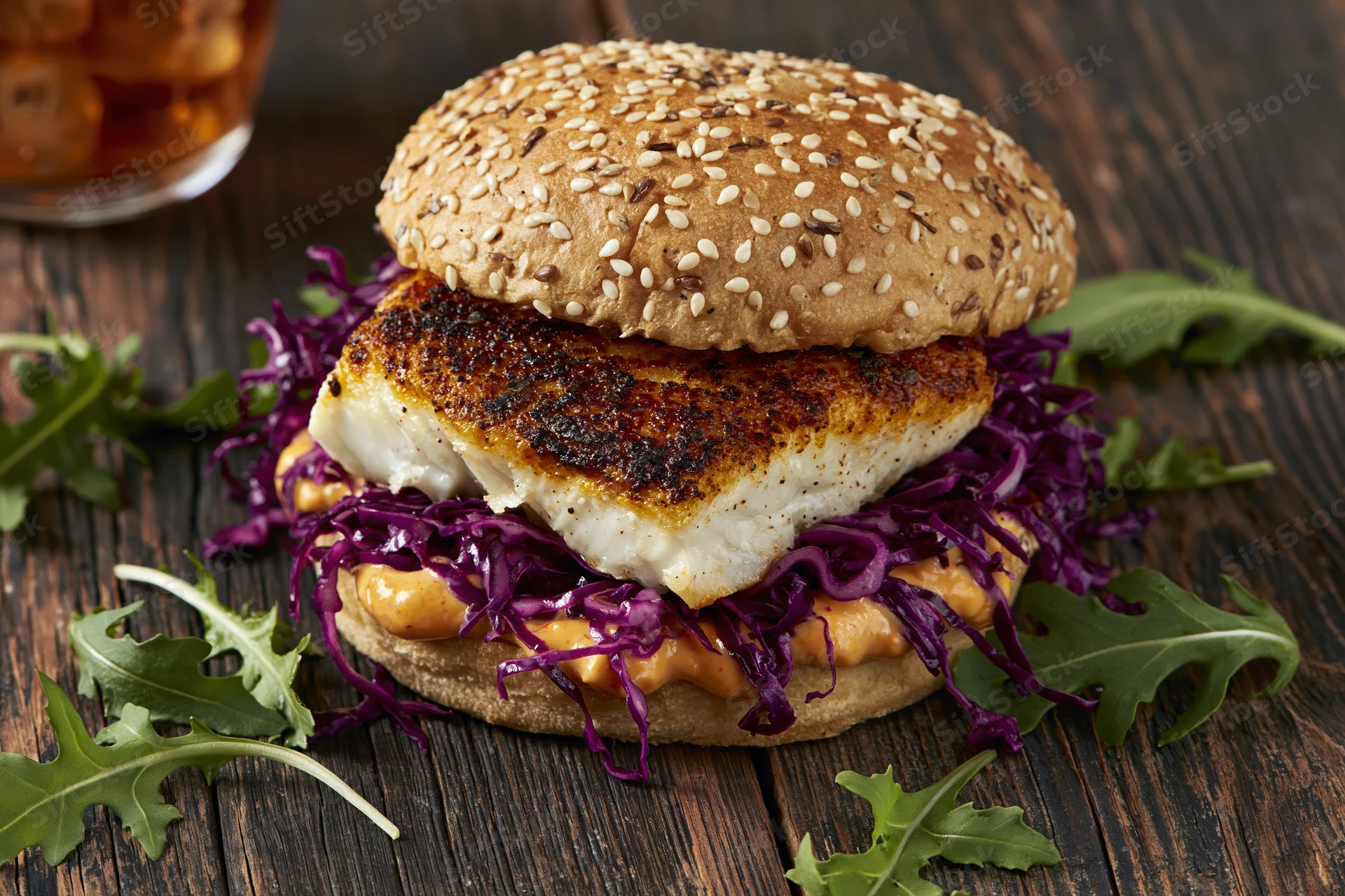 Grilled fish sandwich with purple cabbage and arugula on a sesame seed bun on wooden table