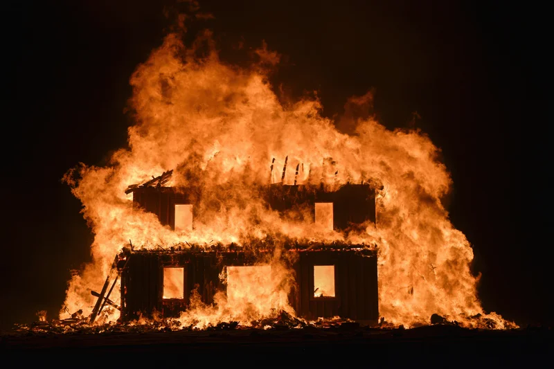 Two-story wooden house fully engulfed in flames at night