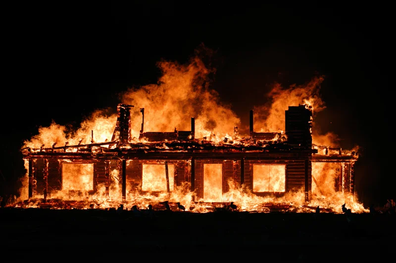 Two-story wooden house fully engulfed in flames at night