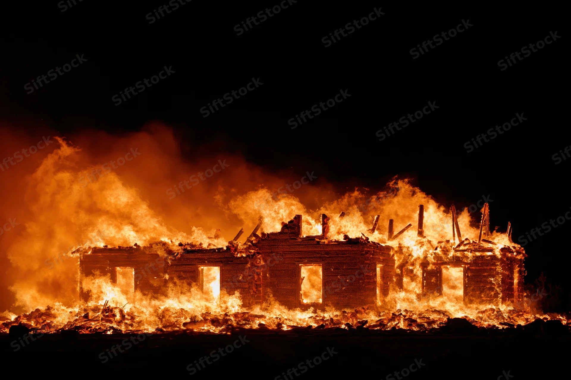 Wooden house fully engulfed in flames at night