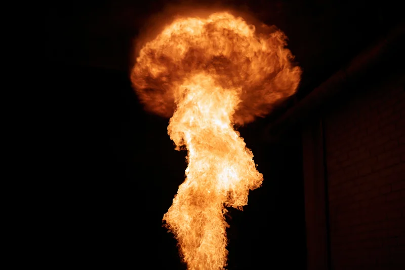 Vertical column of fire rising from a point against dark background near brick wall