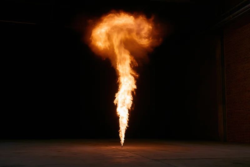 Vertical column of fire rising from a single point in a dark industrial warehouse interior