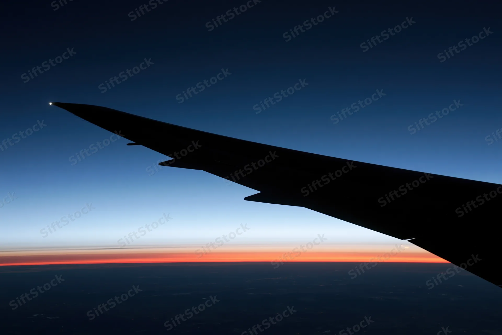 Airplane wing silhouette against twilight horizon from flight window