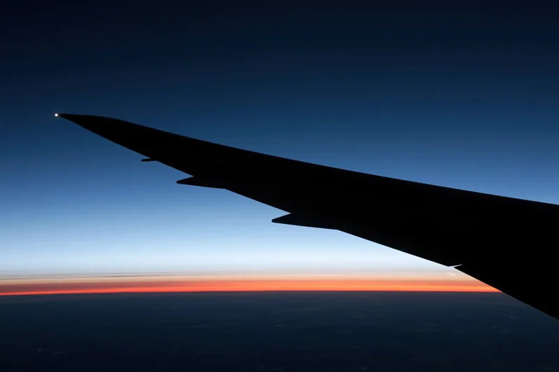 Airplane wing silhouette against twilight horizon from flight window