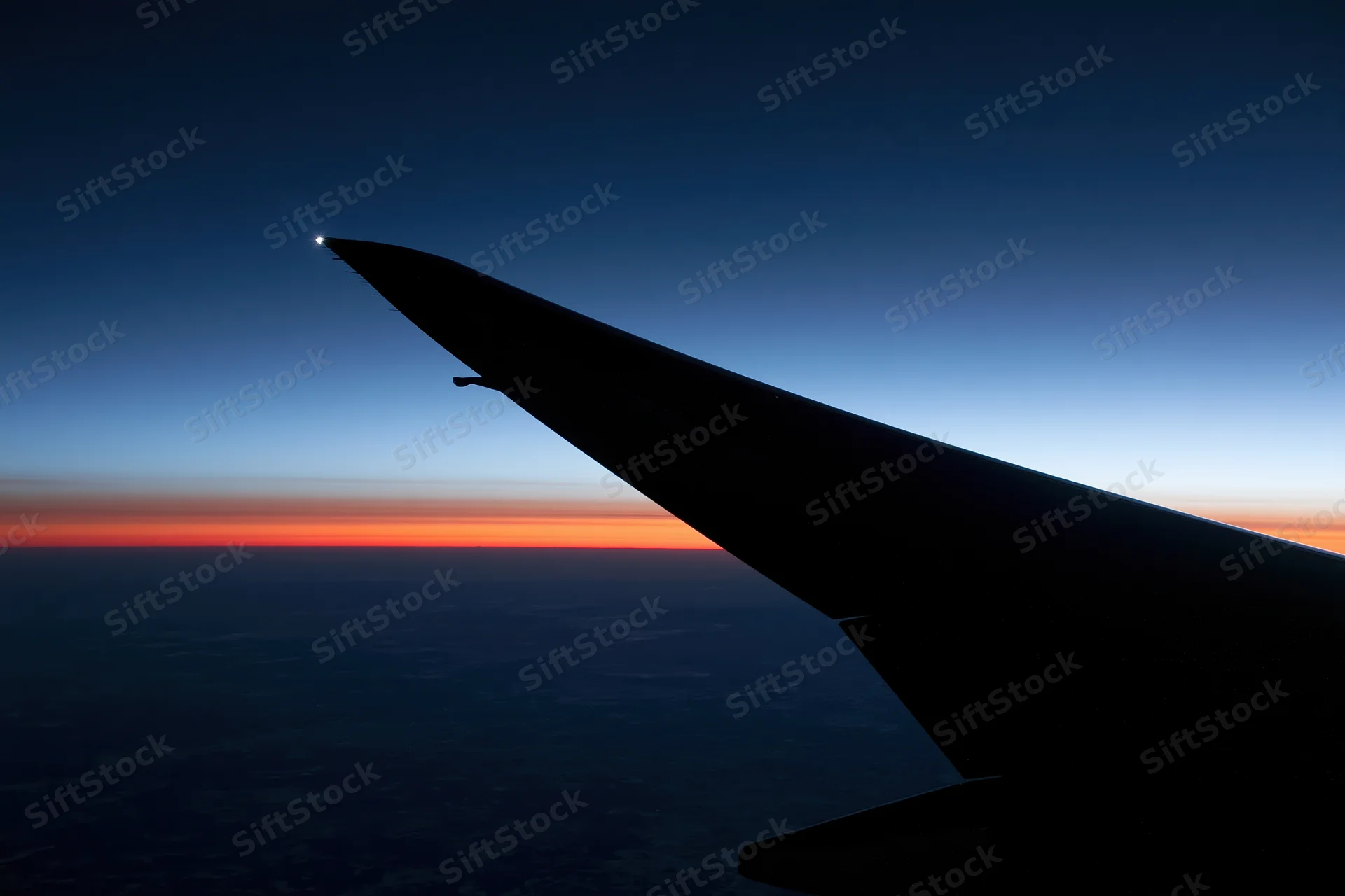 Airplane wing silhouetted against twilight sky with orange horizon line