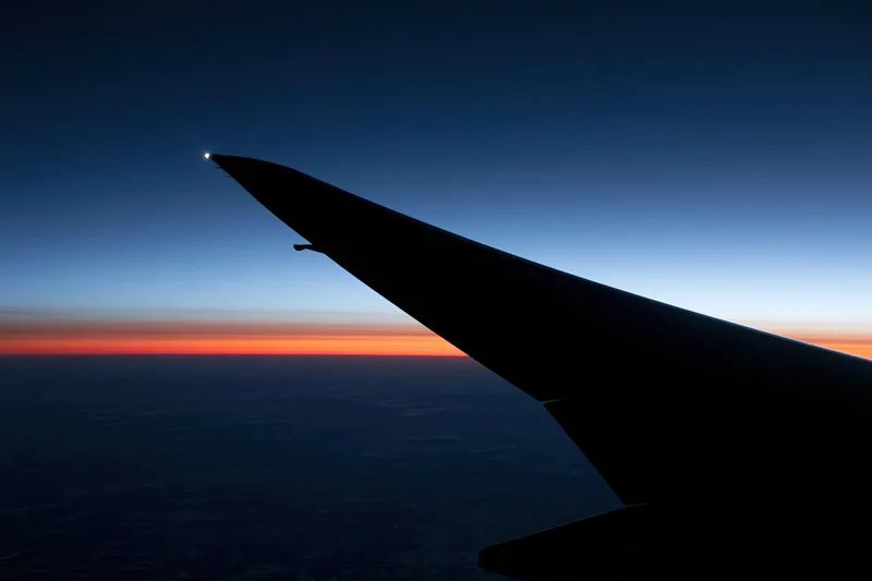 Airplane wing silhouetted against twilight sky with orange horizon line