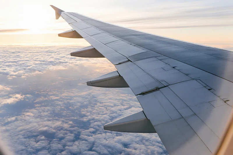 Airplane wing viewed from passenger window above clouds at sunset