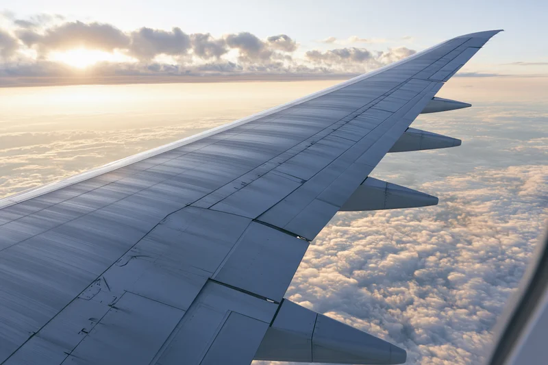 Airplane wing viewed from passenger window during flight above clouds at sunset
