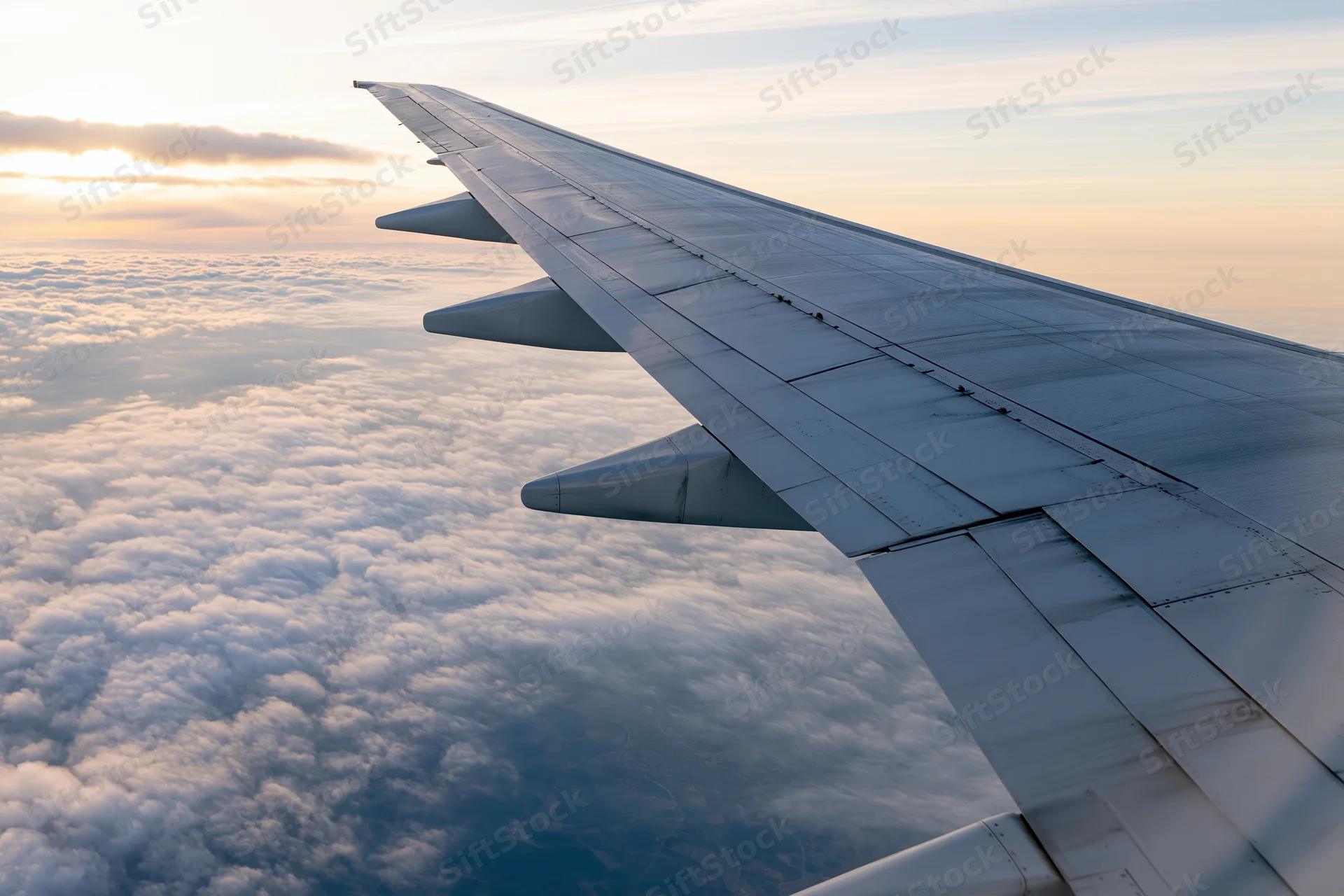 Airplane wing extending over a sea of clouds viewed from a passenger window during cruising altitude at sunset