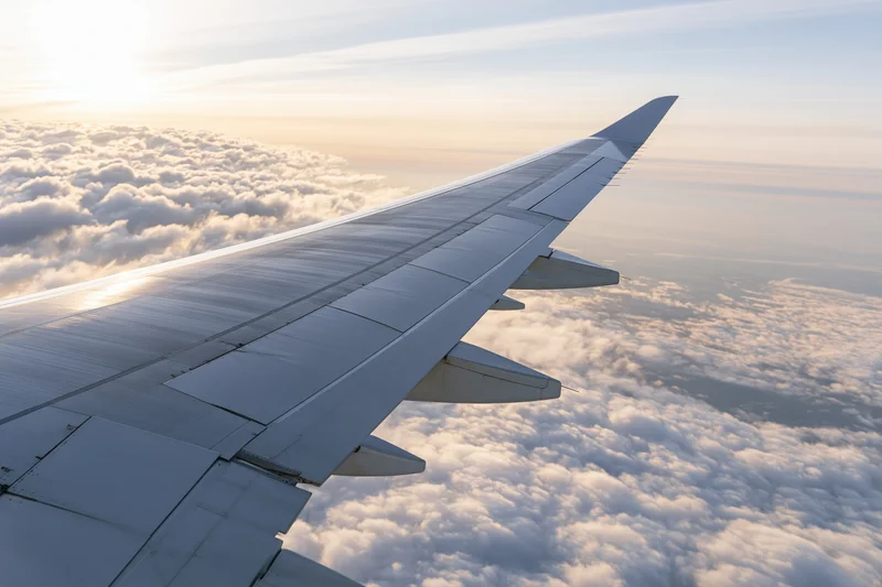 Airplane wing extending over a sea of clouds during sunrise viewed from passenger window