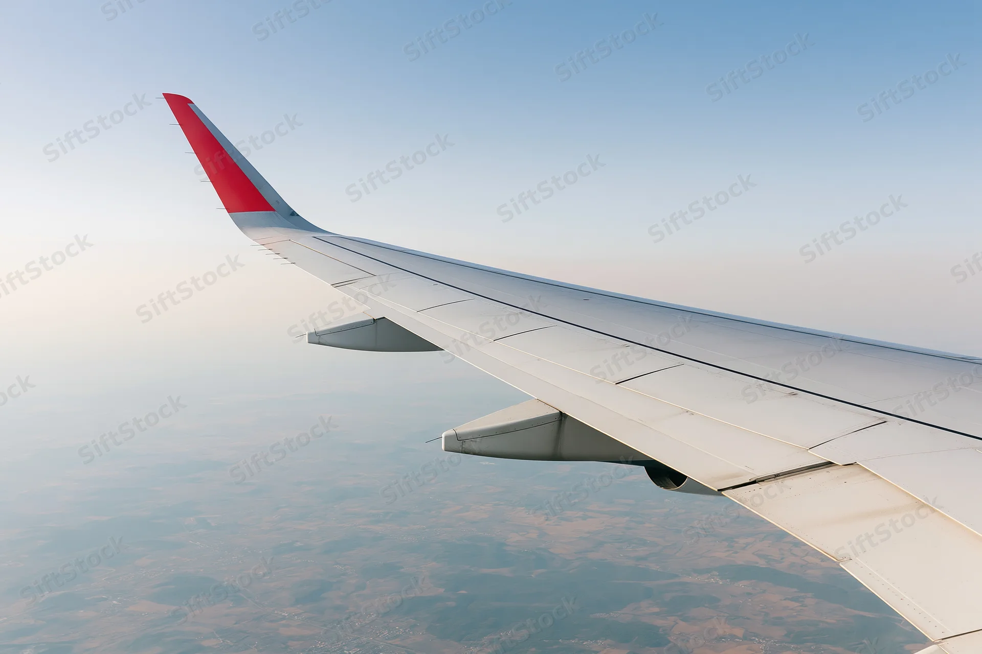 Airplane wing with red winglet viewed from passenger window above landscape