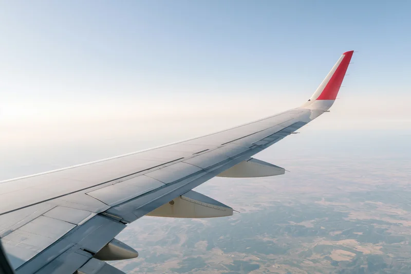 Airplane wing with red winglet viewed from passenger window above landscape