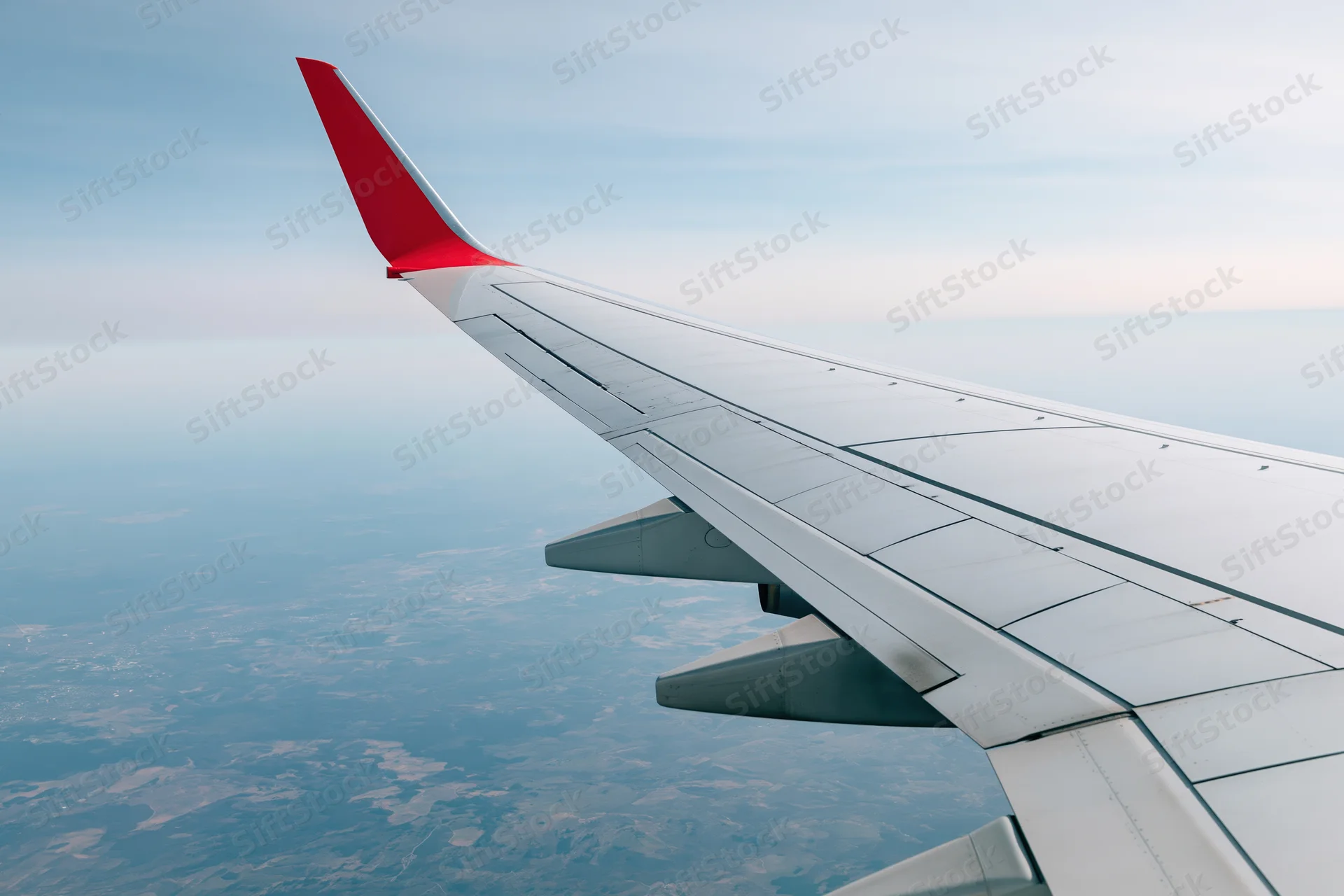 Airplane wing with red winglet viewed from passenger window over landscape below