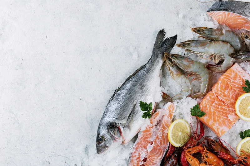 Assorted fresh raw seafood arranged on ice along the right side of a white surface