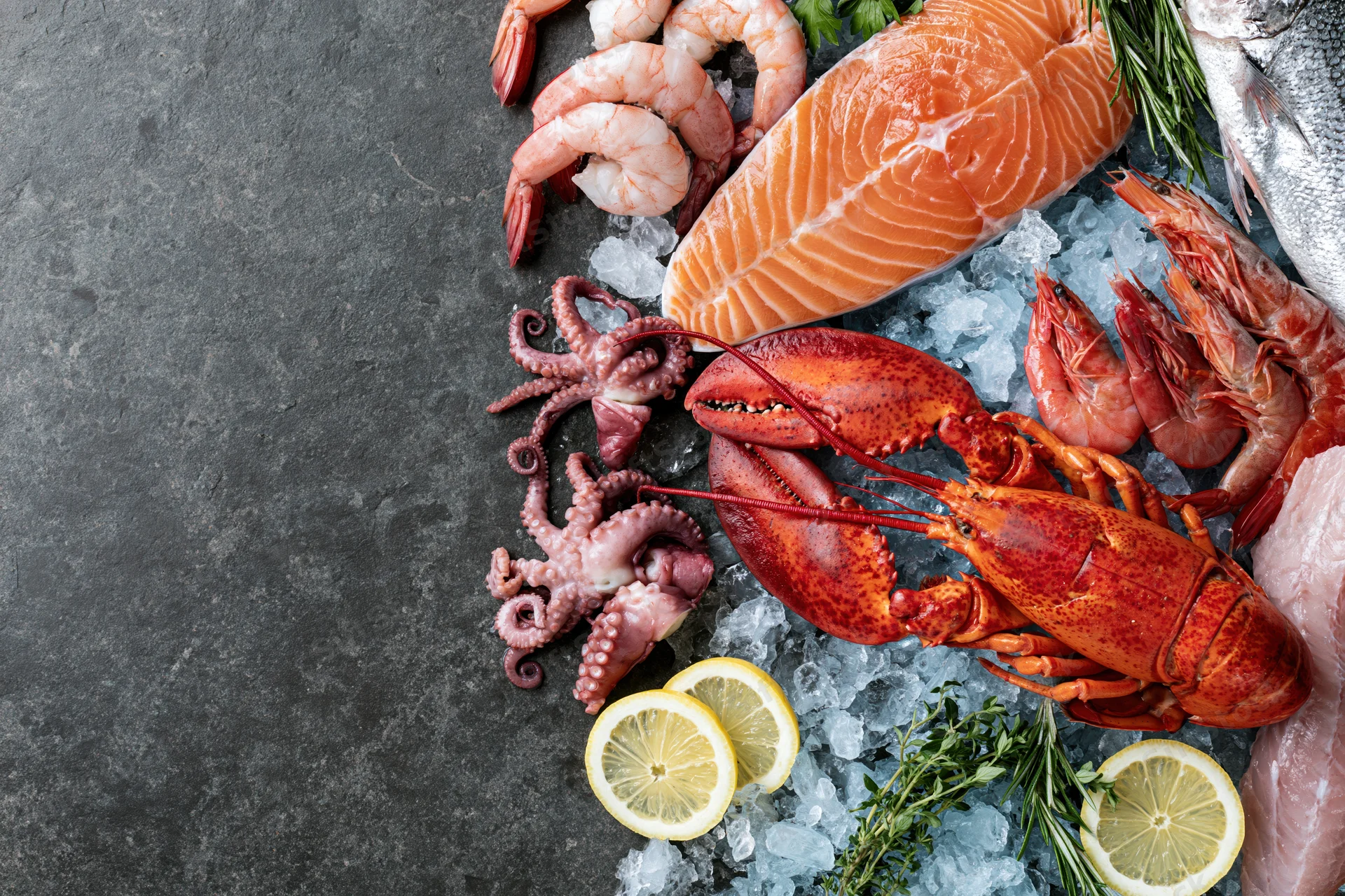 Assorted fresh seafood including salmon, lobster, shrimp and octopus arranged on crushed ice with lemon and herbs on dark surface
