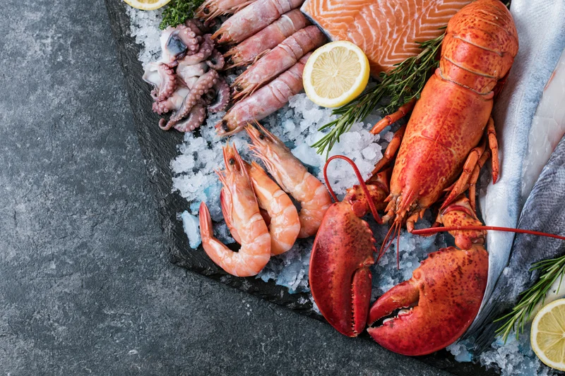 Assorted fresh seafood arranged on crushed ice on a dark stone surface with lemon and herbs