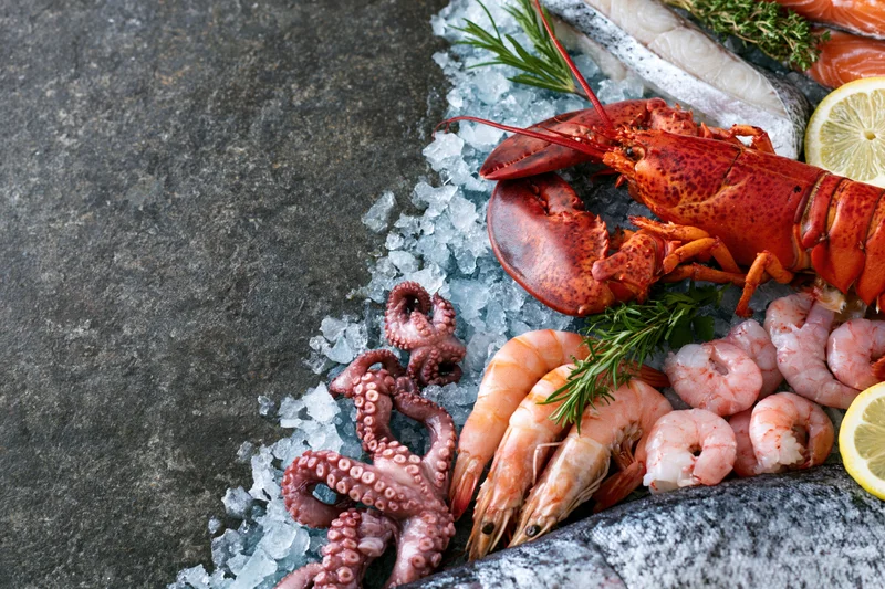 Assorted fresh seafood including lobster, shrimp, octopus and salmon arranged on crushed ice on a stone surface