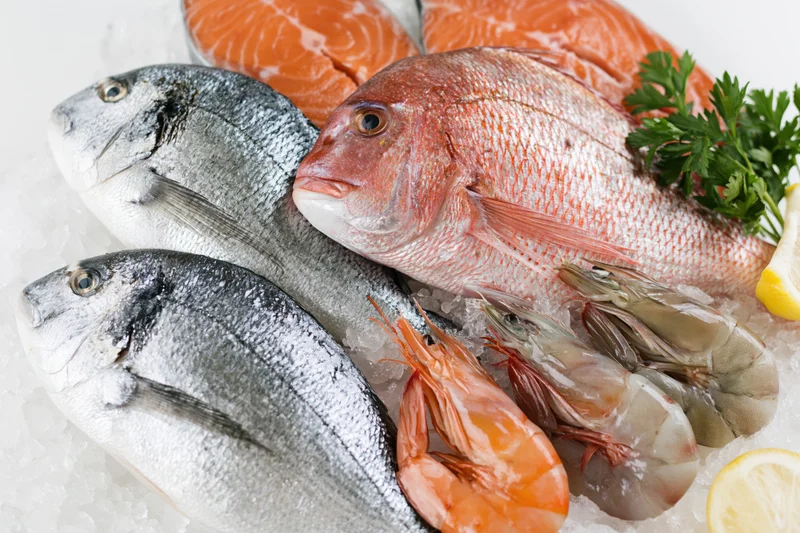 Assorted fresh seafood including whole fish and shrimp arranged on crushed ice with lemon and parsley