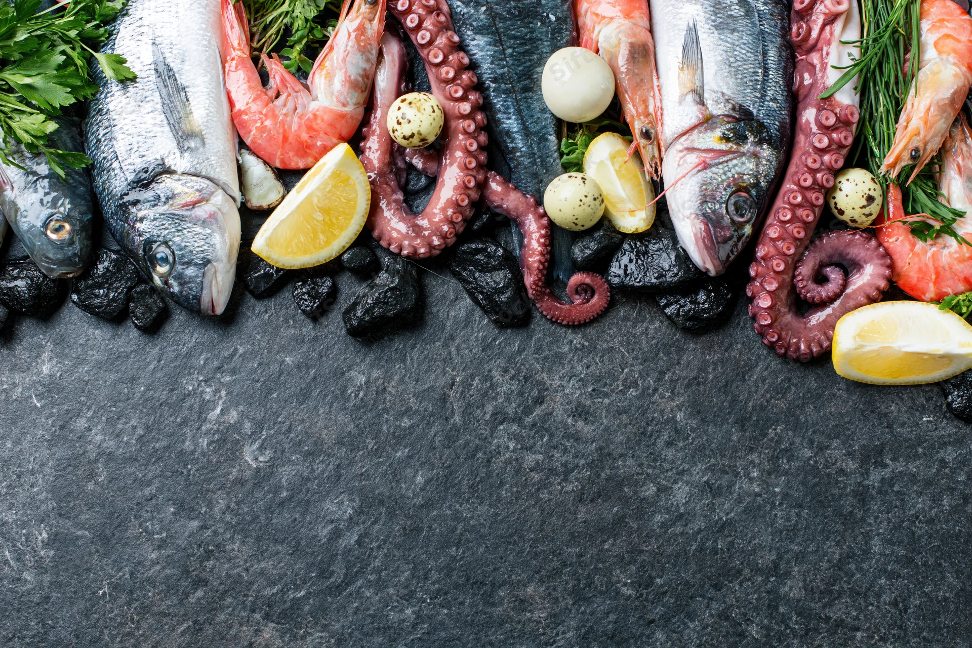 Assorted raw seafood arranged along the top edge of a dark slate surface