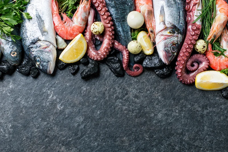 Assorted raw seafood arranged along the top edge of a dark slate surface