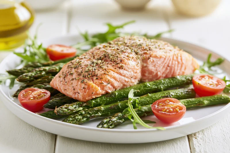 Baked salmon fillet with asparagus and cherry tomatoes on a white plate