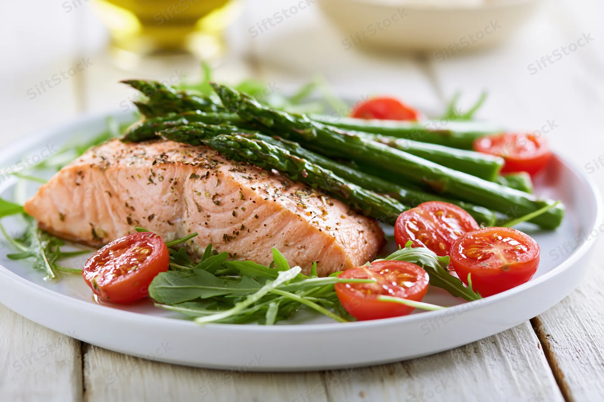 Baked salmon fillet with asparagus and cherry tomatoes on a white plate over wooden table