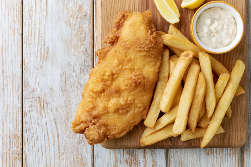Beer-battered fish fillet with golden fries and tartar sauce on a wooden board