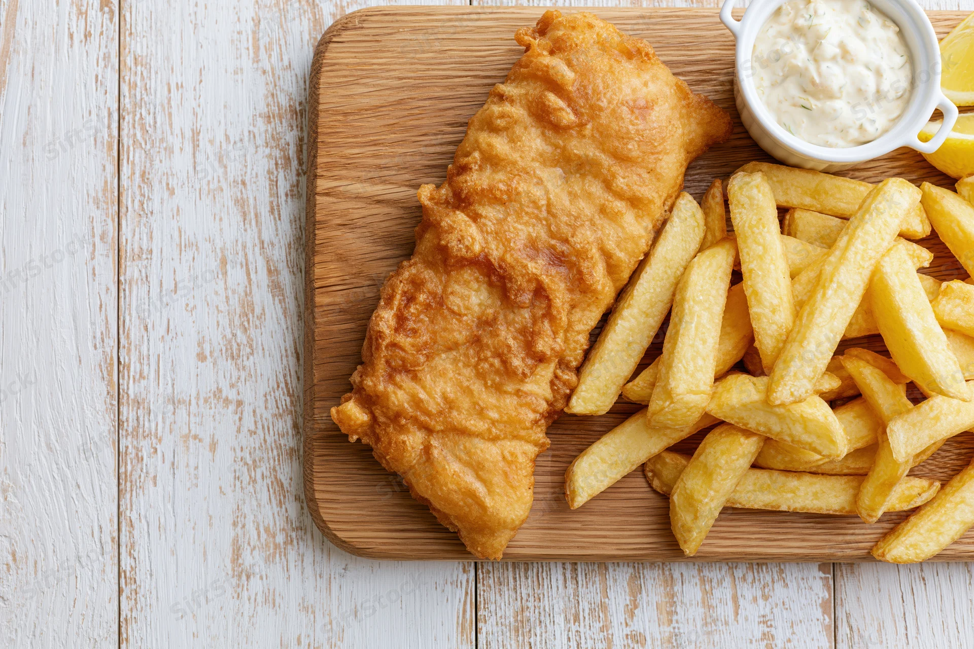 Fried fish fillet with golden french fries and tartar sauce on a wooden cutting board